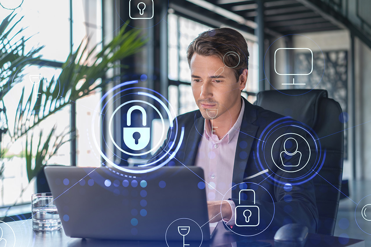 Handsome businessman in suit at workplace working with laptop to defend customer cyber security. Concept of clients information protection and brainstorm. Padlock hologram over office background.